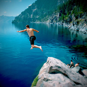 A man jumping of a rock into a tree lined lake
