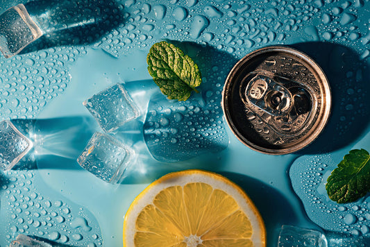 A photo of a can, a slice of lemon, and a mint leaf on a table with ice